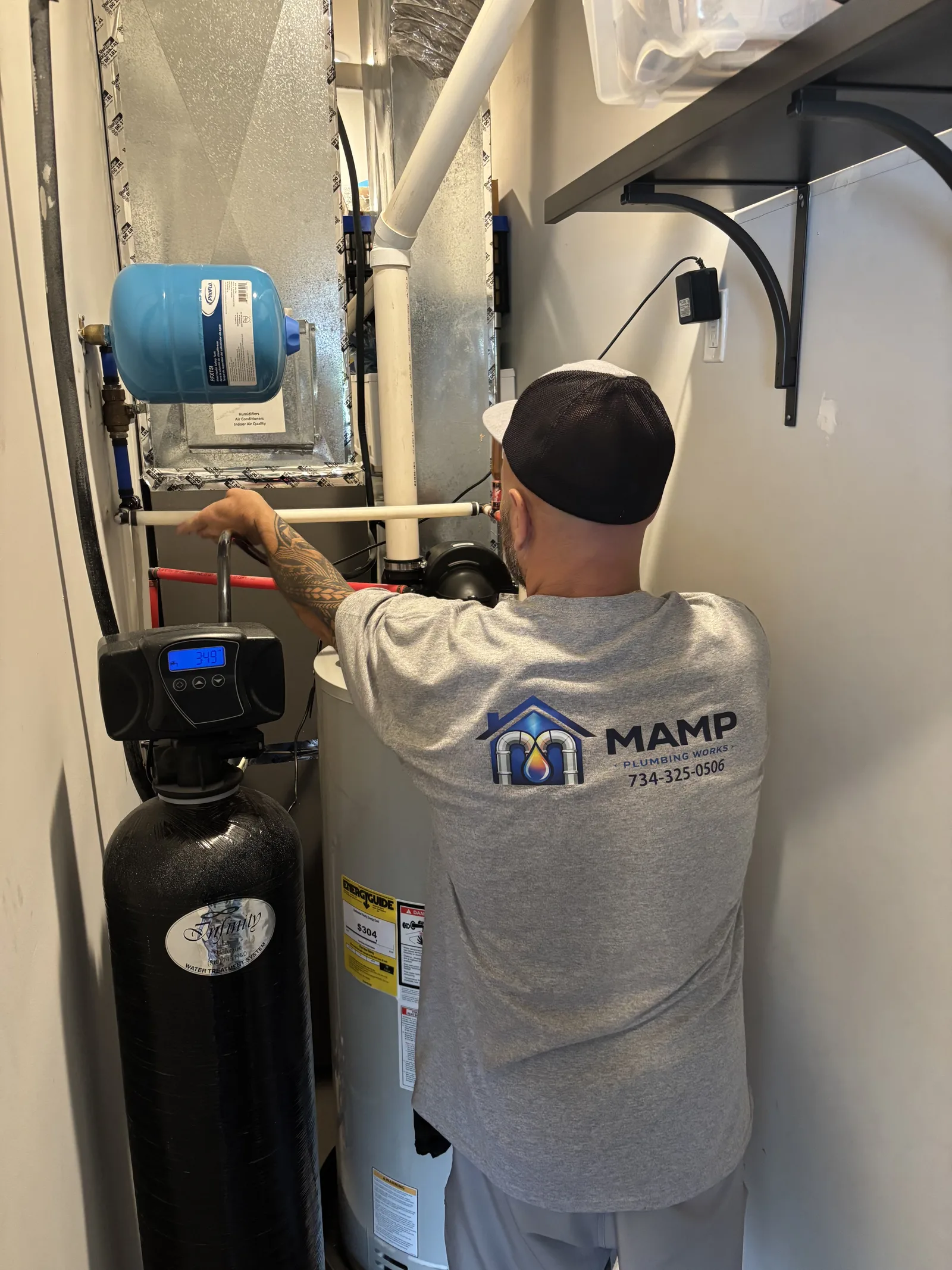 David Mamp adjusting supply piping between a water softener and a water heater in a home utility closet
