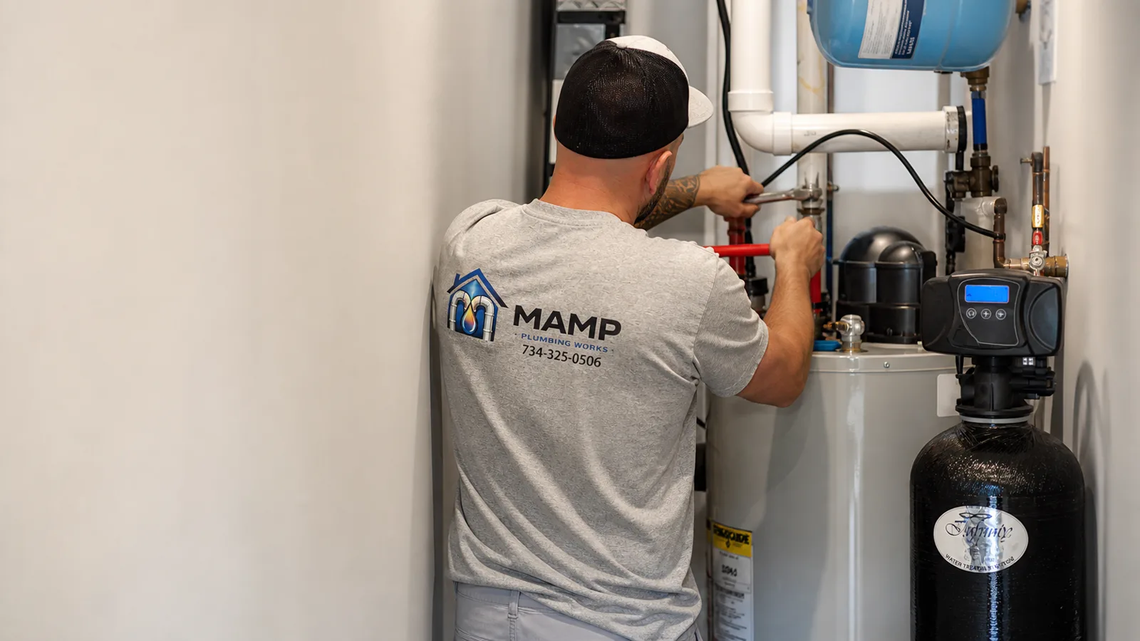 David Mamp tightening the water connections on a newly installed residential water heater beside a softener tank and expansion tank